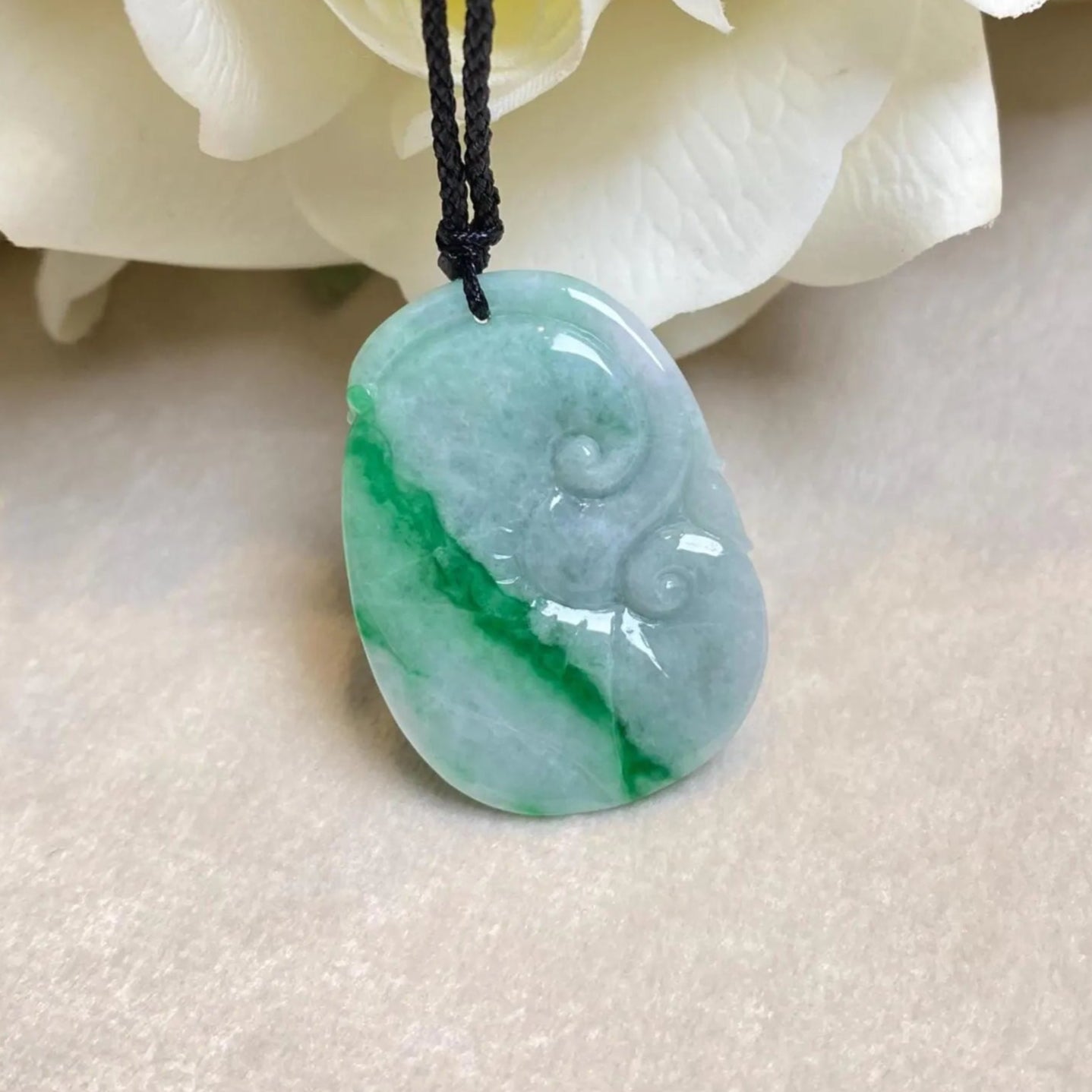 Green jade pendant on a black cord with white flowers in the background