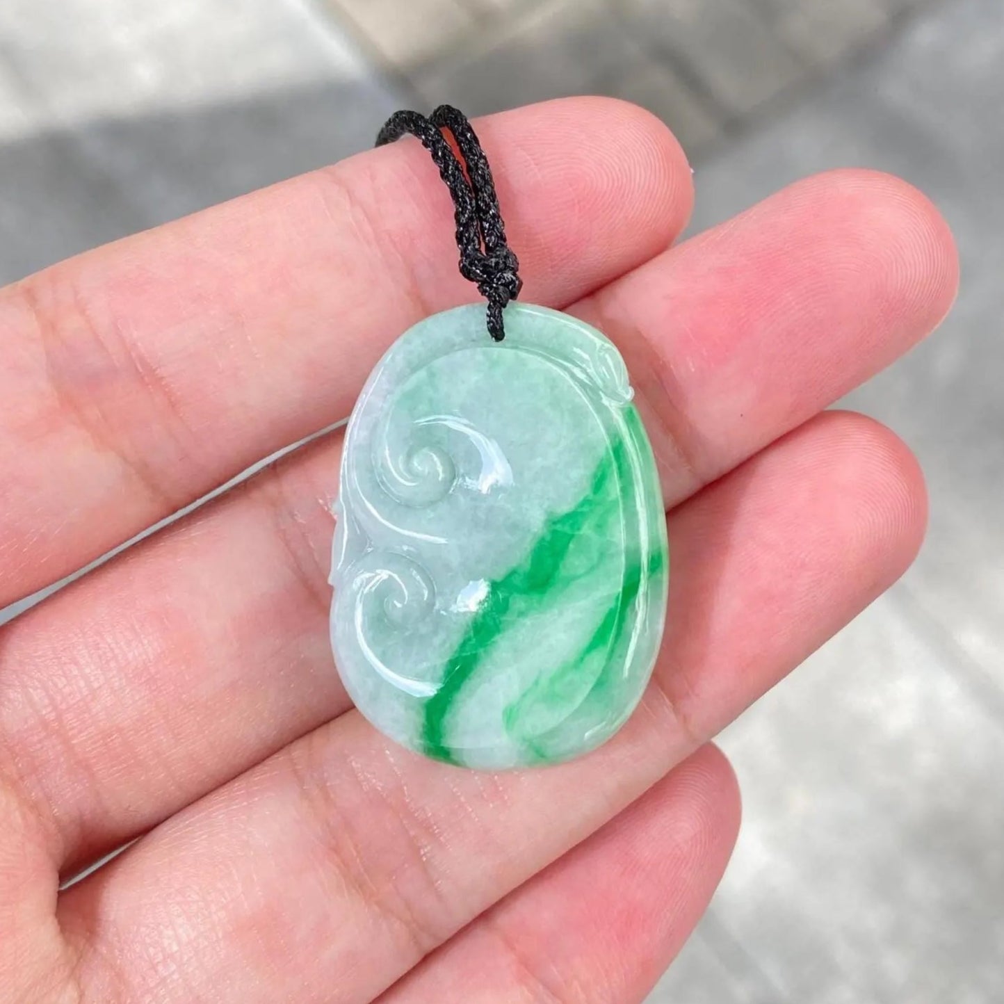 Green jade pendant held in a hand with a blurred background