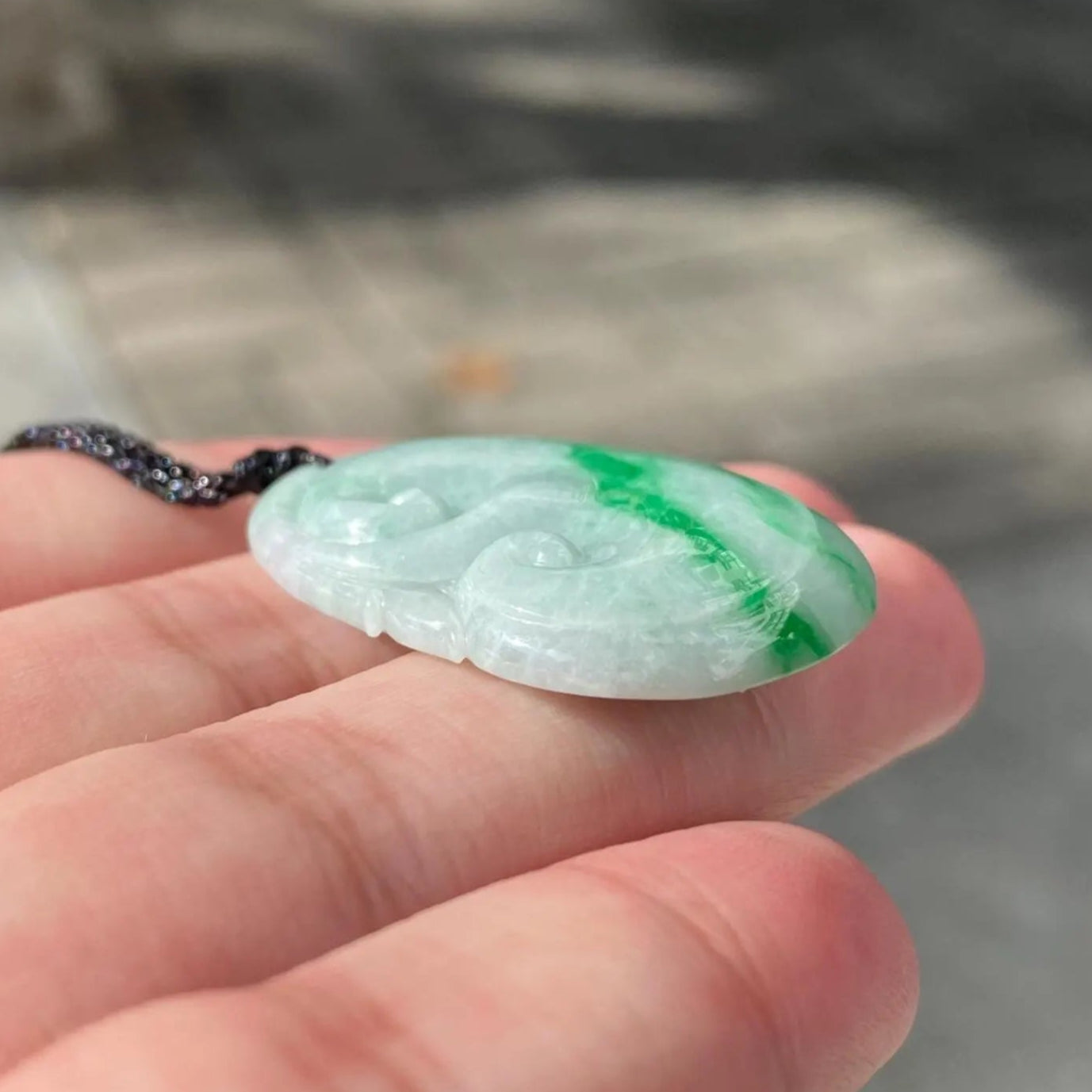 Green jade pendant held in a hand with a blurred background